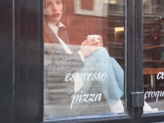 A woman looking through the window of a coffee shop as she holds a mug in her hands