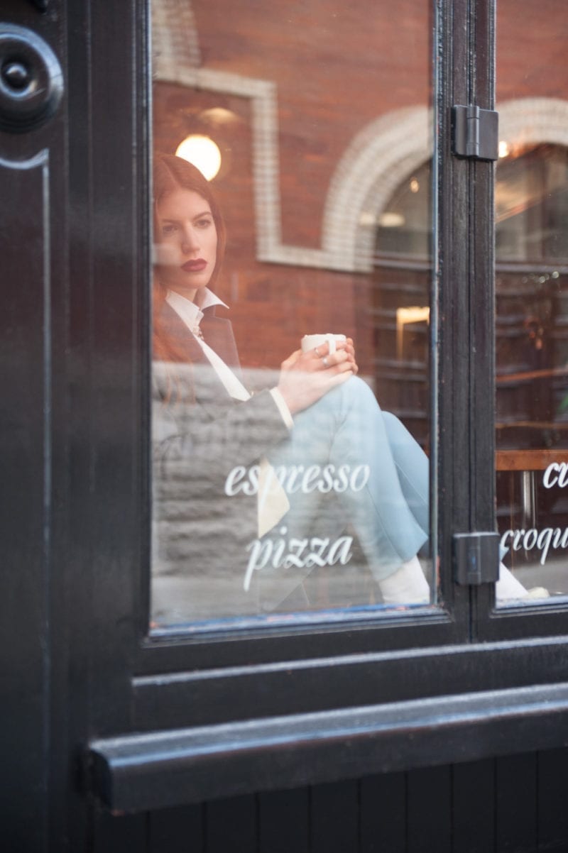 A woman looking through the window of a coffee shop as she holds a mug in her hands