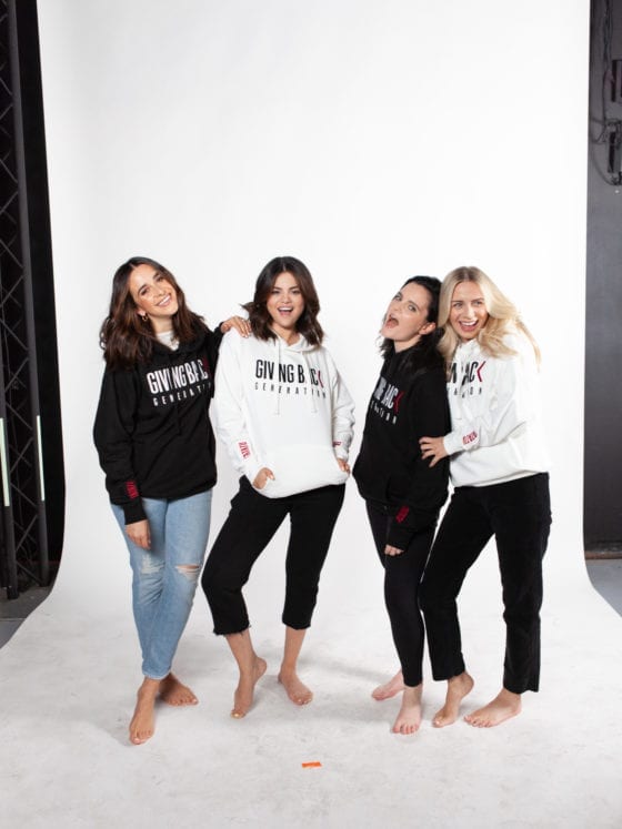 Four women in hoodies standing and smiling and laughing toward the camera