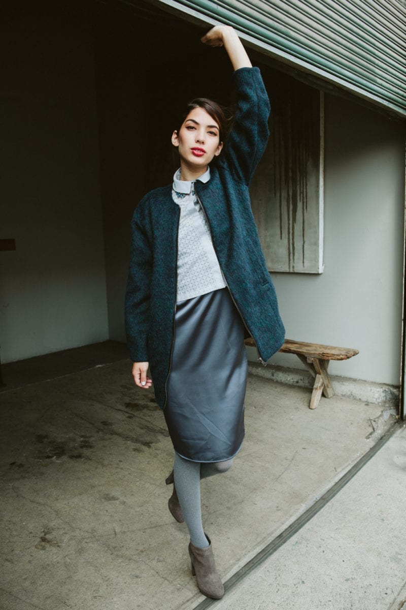 A woman in a sweater and skirt holding up a garage door while staring at the camera