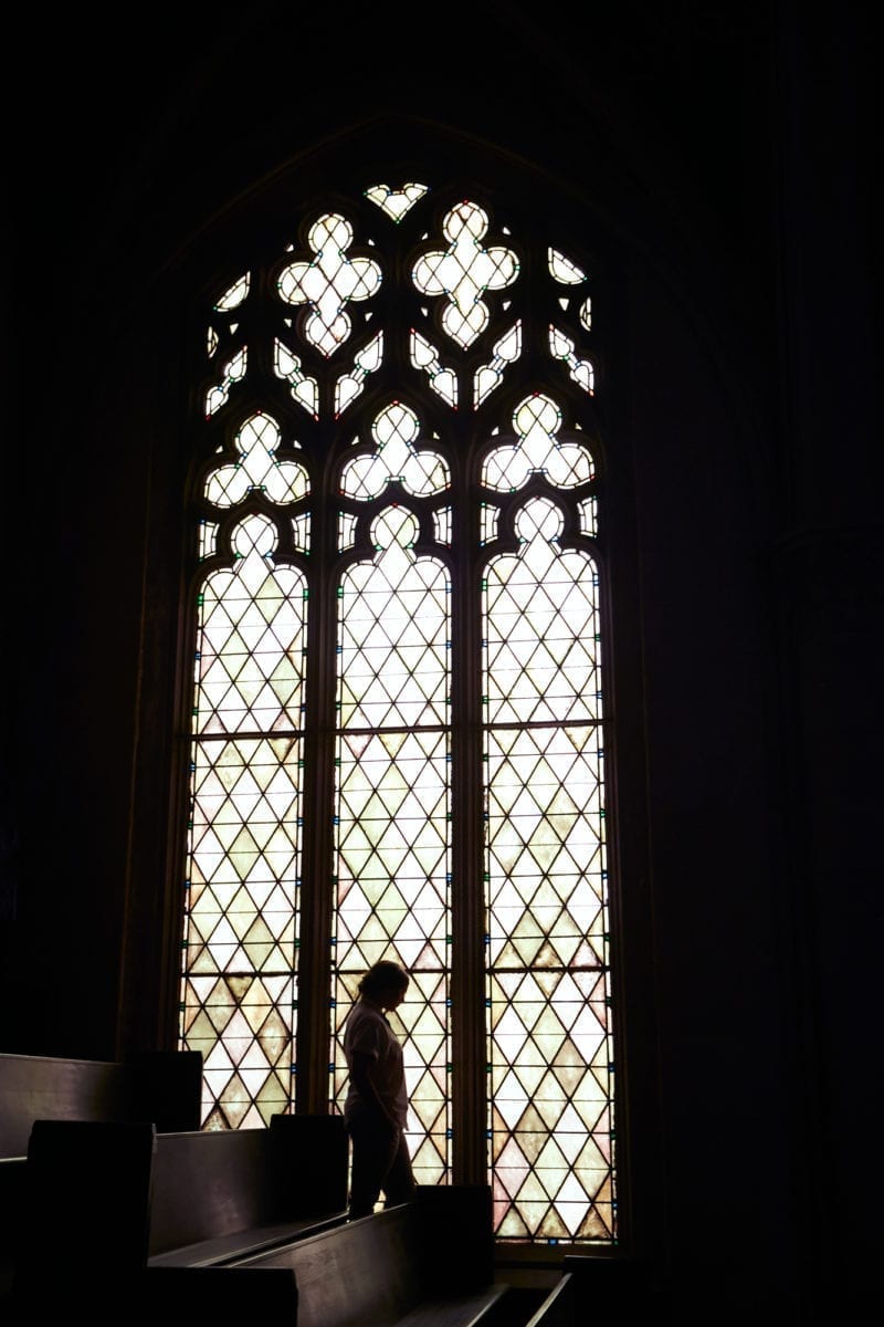 A black and white photo of a woman standing in front of a church chapel window