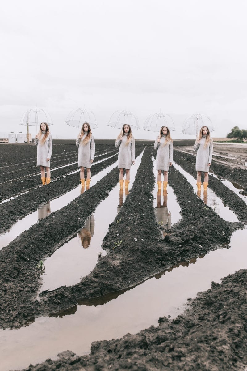 Five identical woman standing in the trenches of a field with umbrellas