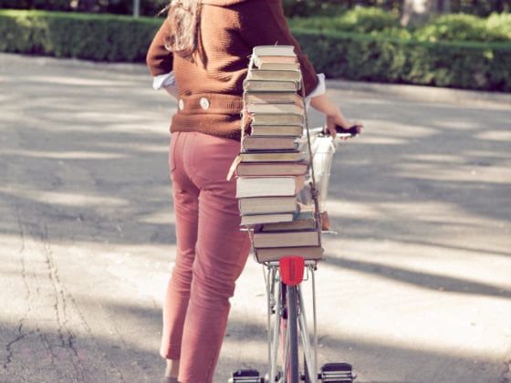 A picture of a girl standing next to a bicycle with books on her seat