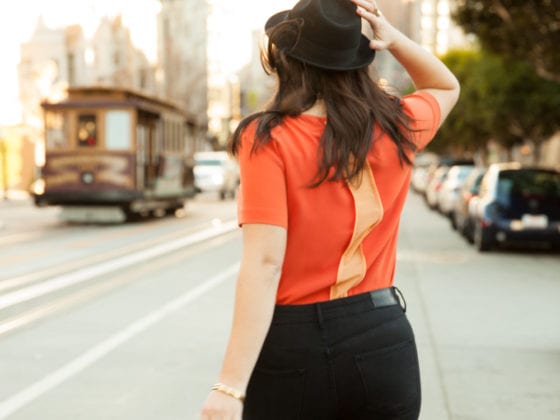 A woman holding her hat as she walks down the street
