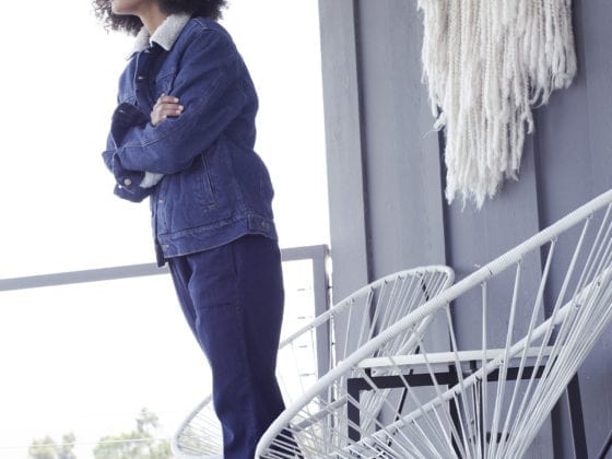 A woman in an all denim outfit leaning forward as she stands on the porch
