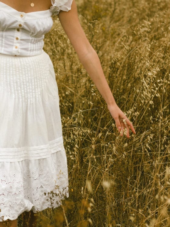 An up close shot of a woman in a dress walking through a field