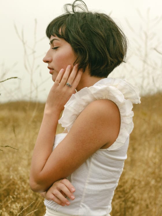 A side profile of a woman standing in a field with her eyes closed and her hand to her face