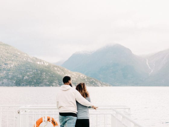 A woman and man standing at the edge of a boat looking out into the mountains in the distance