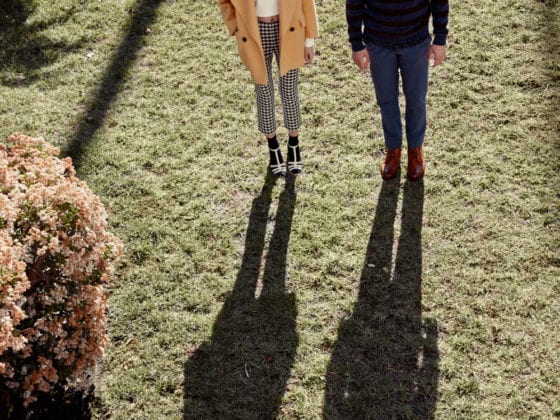 A man and woman standing outside on grass looking up at the camera lens