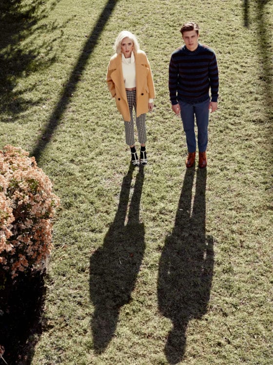 A man and woman standing outside on grass looking up at the camera lens