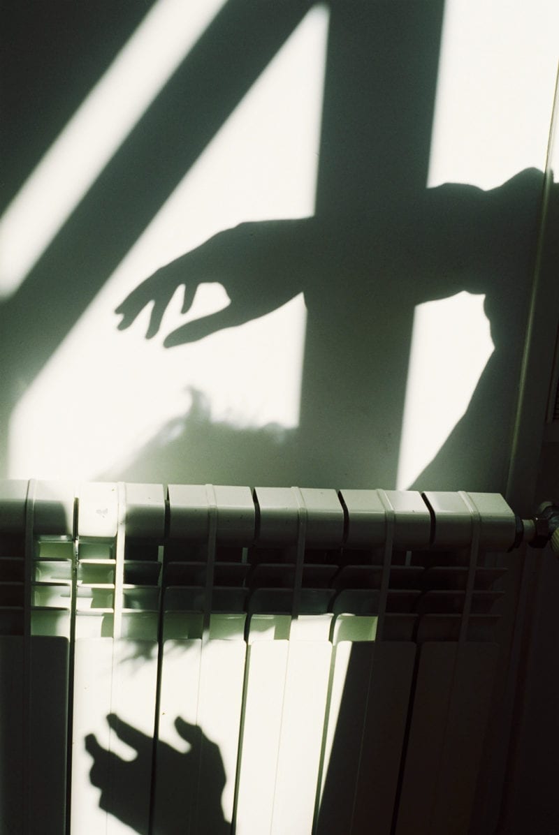 An image of the shadow of a person learning over a wall heater