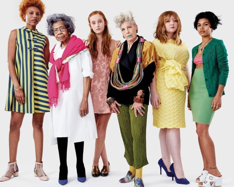 A group of diverse women in multiple bright colors standing and staring in the camera without smiles