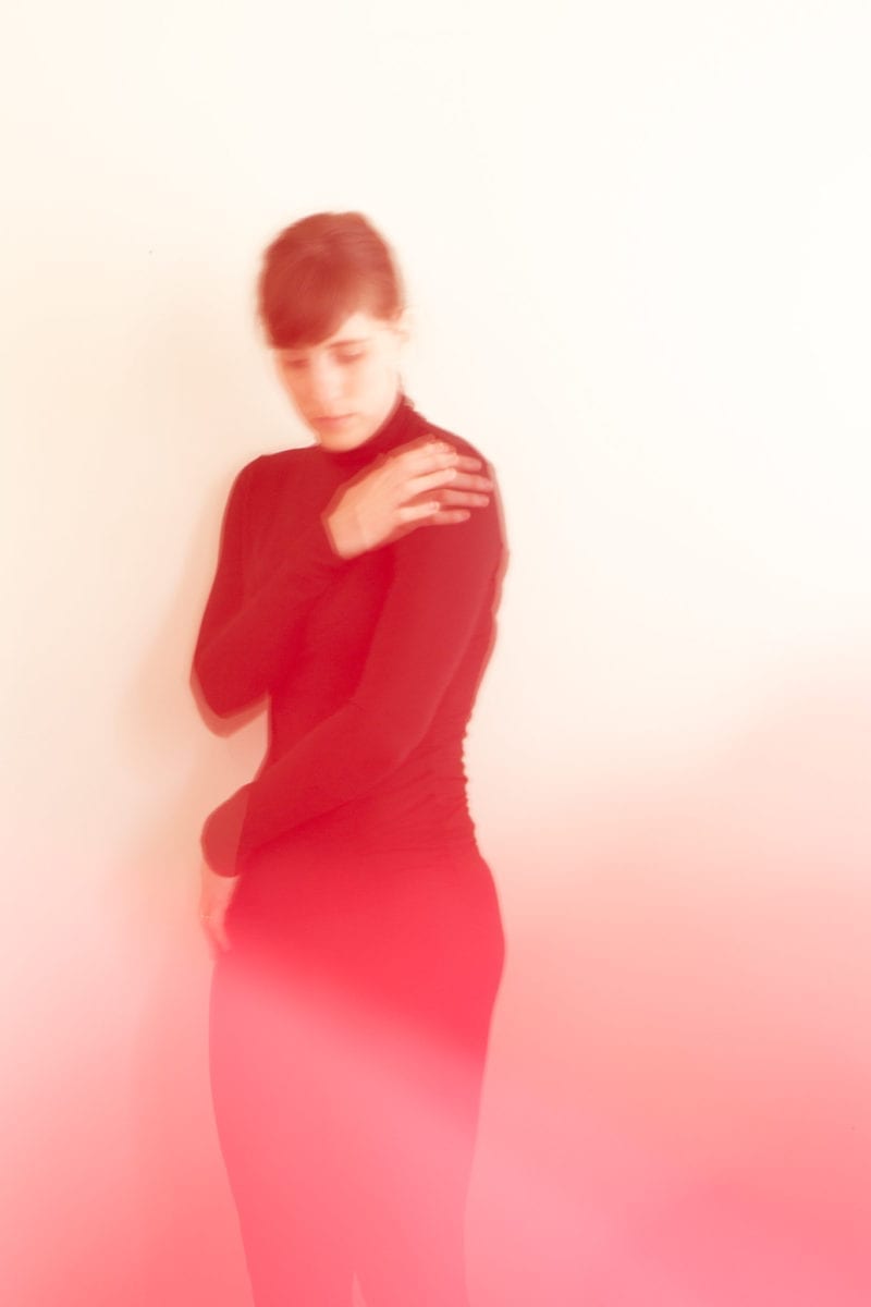 A blurry image of a woman in all black as she wraps her arms around herself