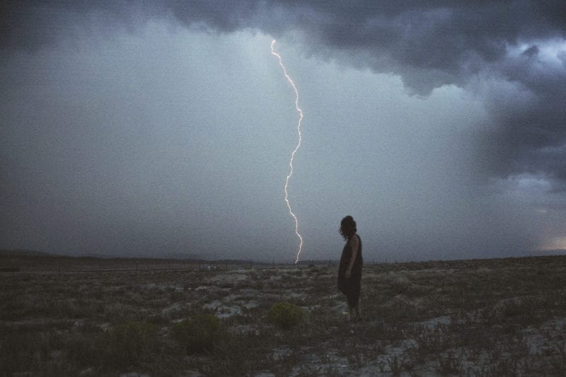 A woman standing in a field with lightning