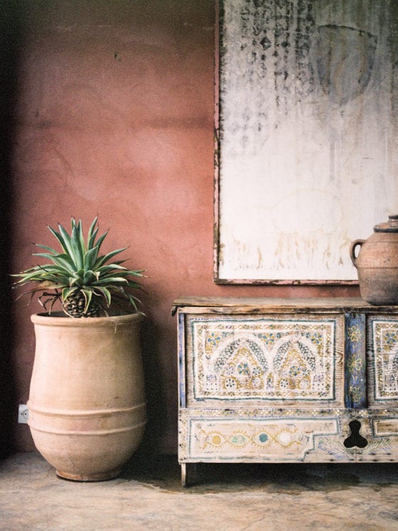 A piece of art, a dresser and a plant against a wall