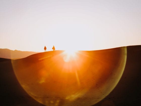 Two people walking through a desert as the sun sets behind them