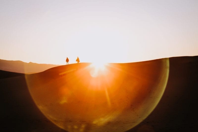 Two people walking through a desert as the sun sets behind them