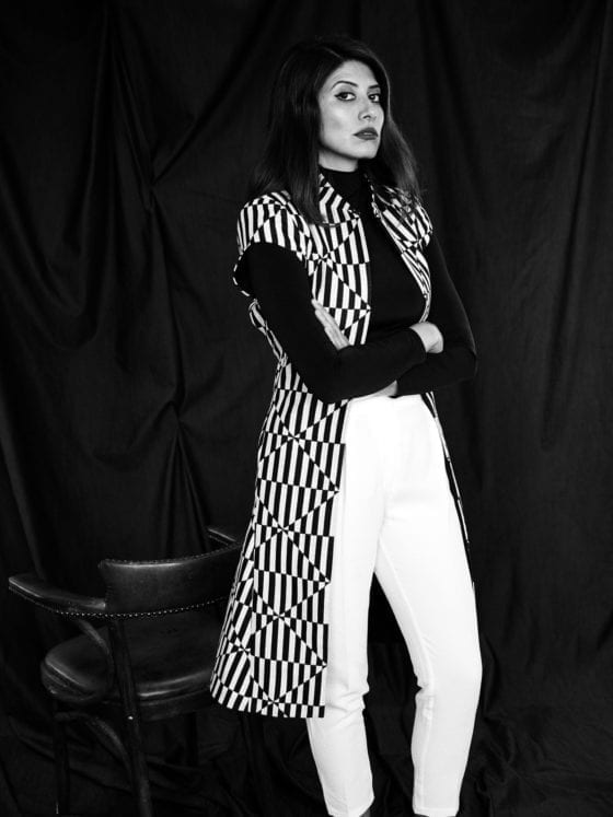 A black and white photo of a woman in white pants standing in front of a black background