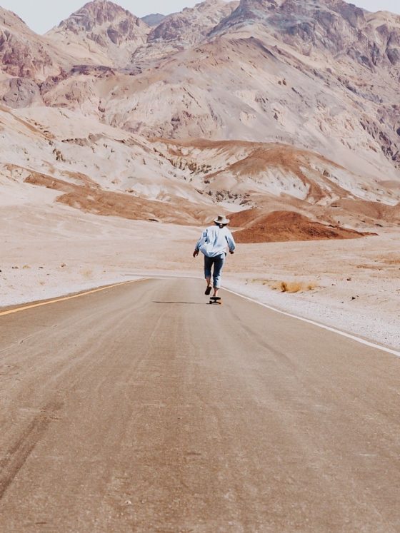 A woman skating on an empty road toward the mountains in the background