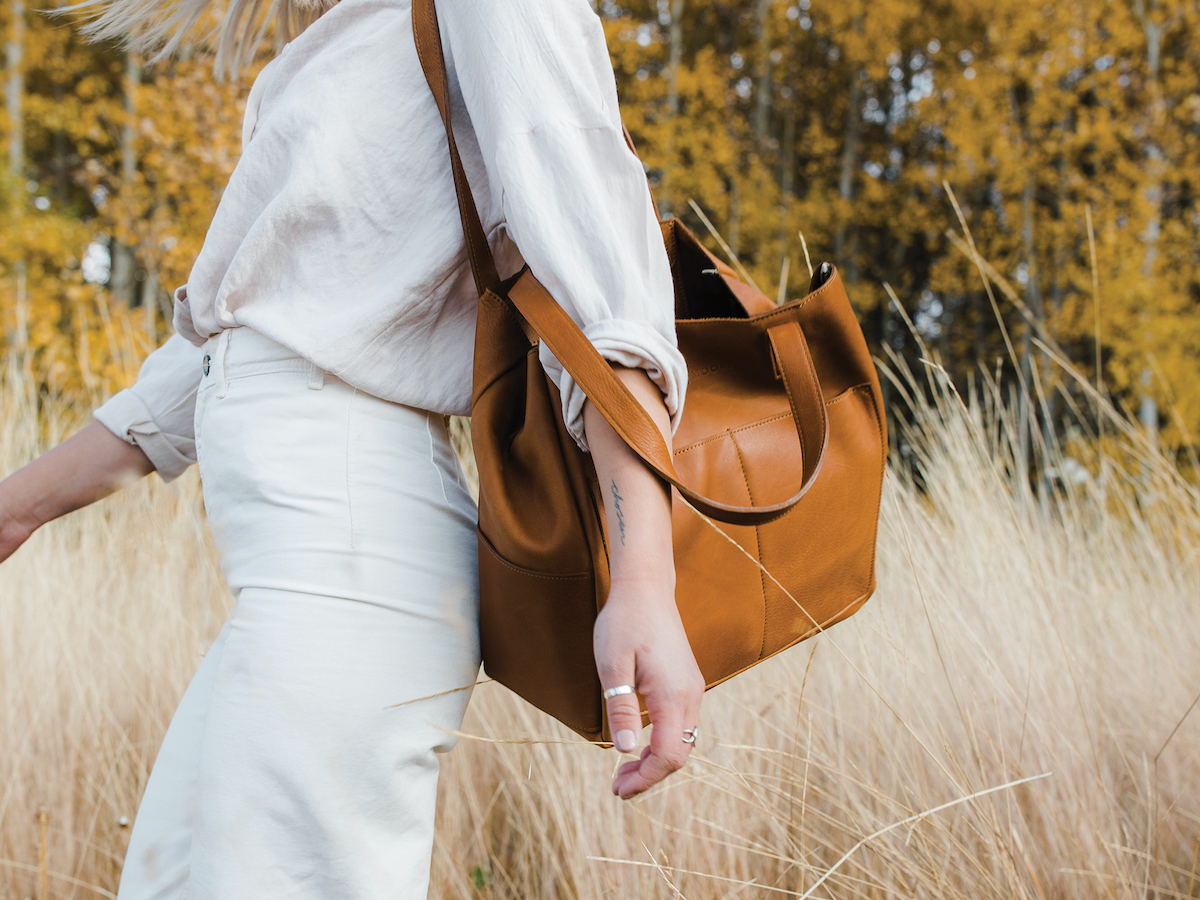 A woman walking through a field with a leather bag