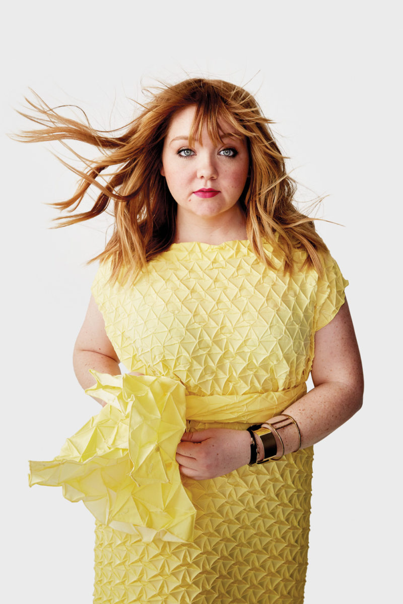A woman in a yellow dress standing as the wind blows her hair