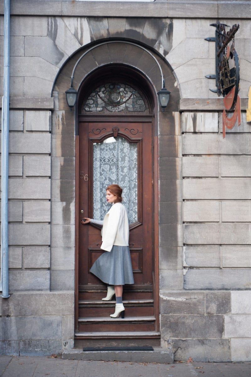 A woman standing outside a door as she hold the handle to enter