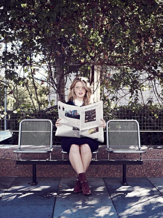 A woman holding a newspaper as she sits on a bench reading