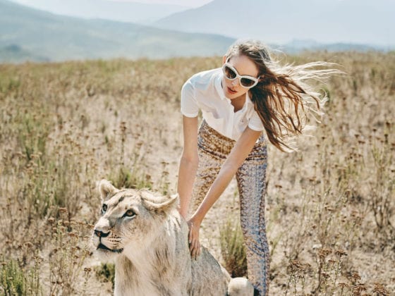 A woman in a grassy plain petting a tiger