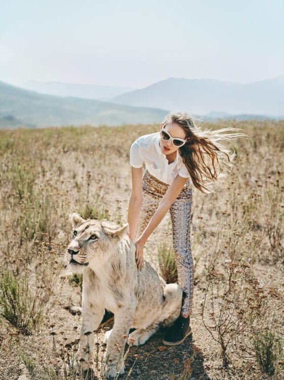 A woman in a grassy plain petting a tiger