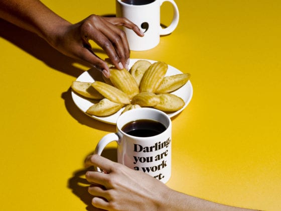 Two people reaching for cups of coffee with a table of cookies in the center