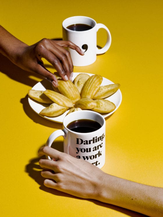 Two people reaching for cups of coffee with a table of cookies in the center