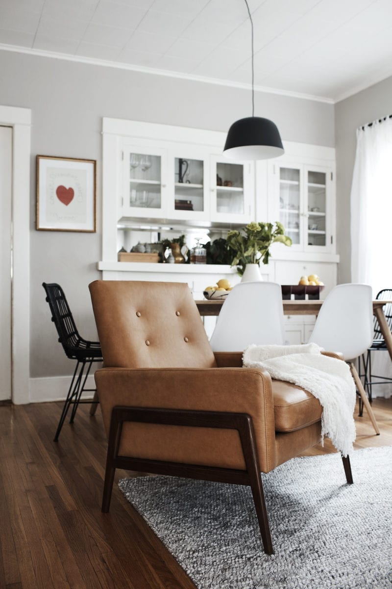 A brown leather chair with a white throw blanket on it and a kitchen table behind it