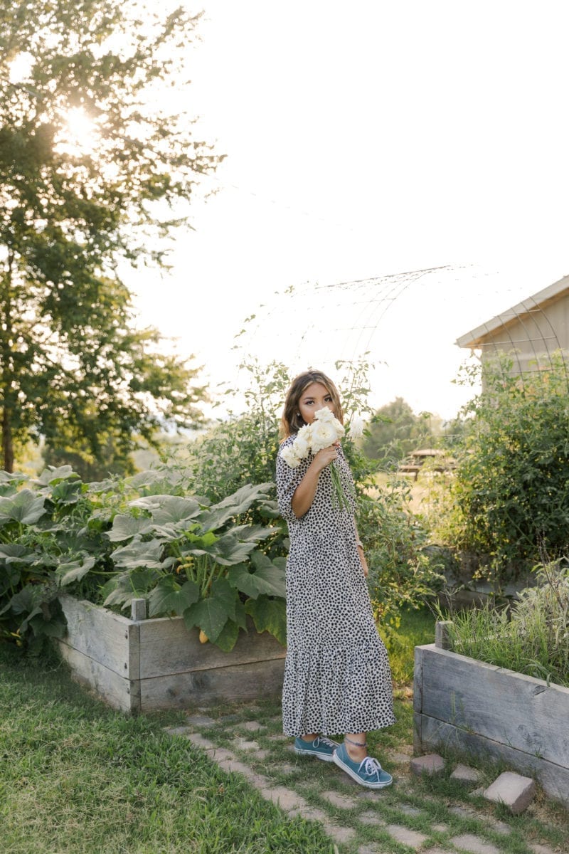 A woman in a dress and sneakers smelling flowers
