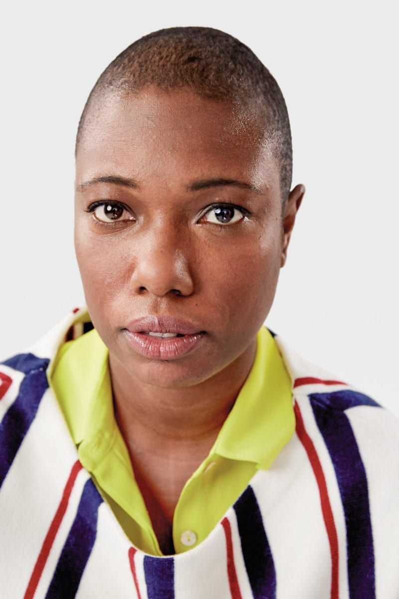 A bald woman in a stripped shirt looking toward the camera