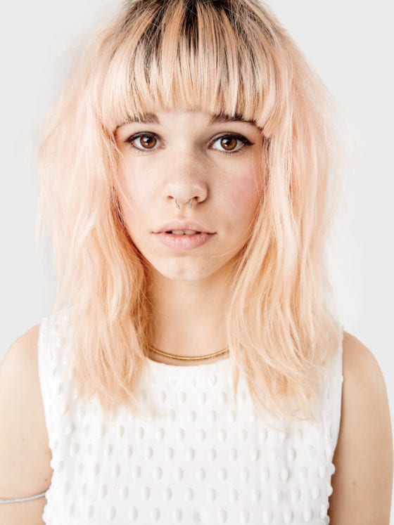 A close up of a woman's face with pink hair and bangs