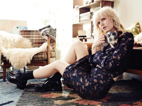 A woman holding a pet pig as she sits on the floor in front of a couch