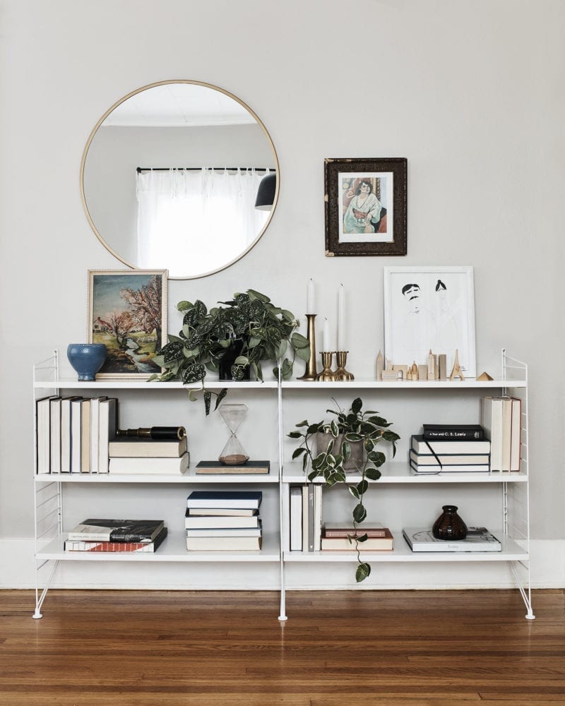 A book stand with greenery on it and a mirror hanging on the wall behind it