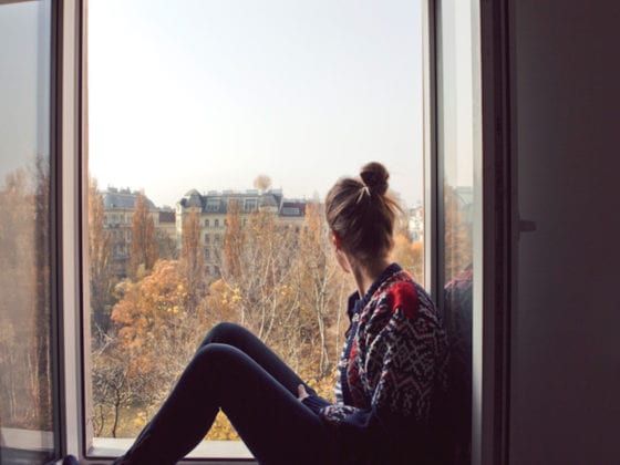 A woman seated in a window sill looking out at the skyline