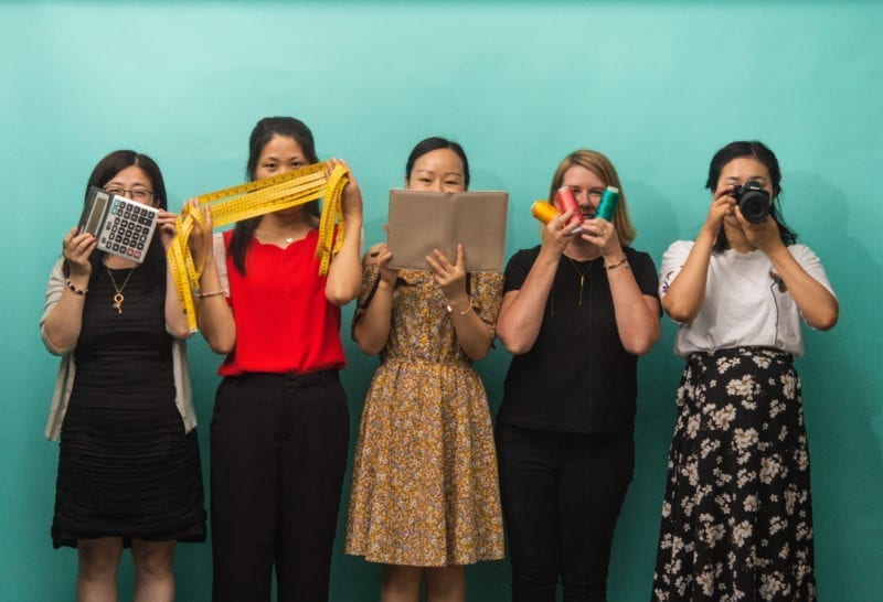 Five women holding up items th cover their faces
