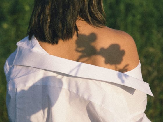 A woman with an off-the-sholder shirt with the reflection of a flower on her shoulder
