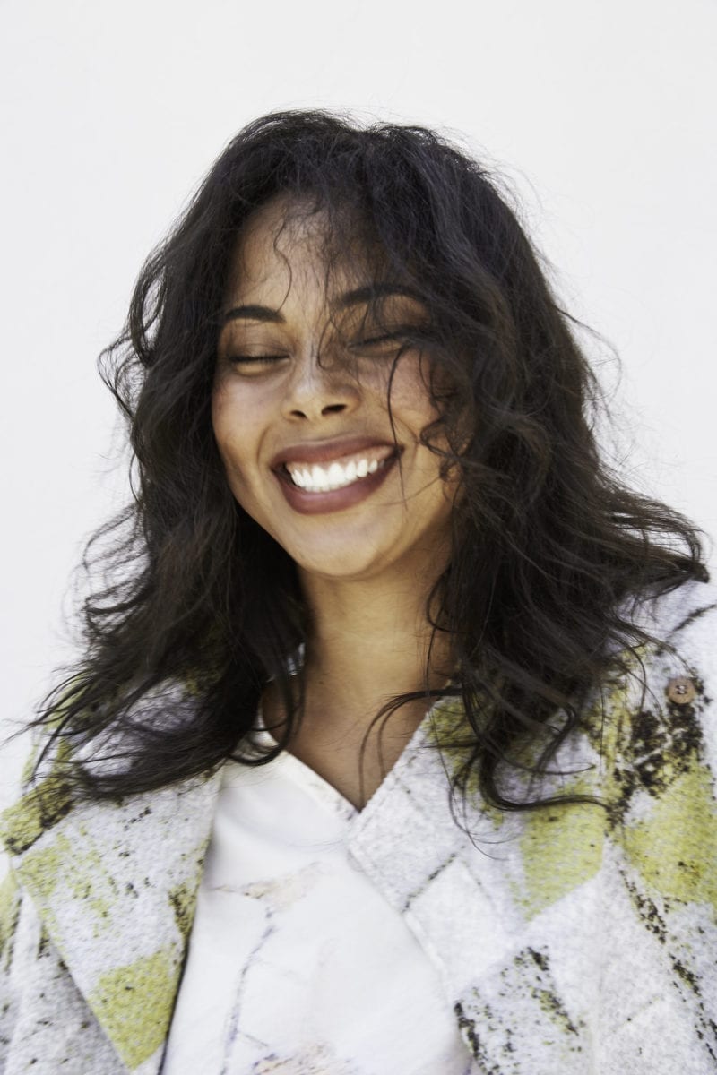 A smiling woman with her hair tossed in front of her closed eyes