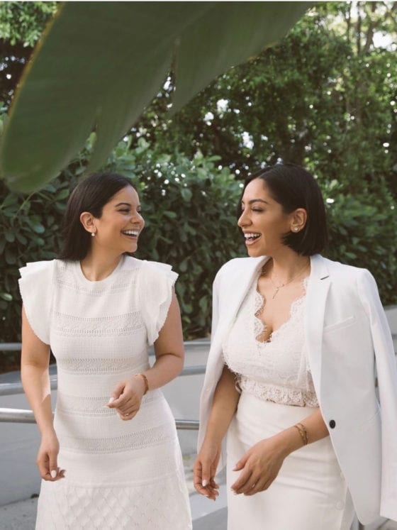 Two laughing women standing outside and wearing all white outfits