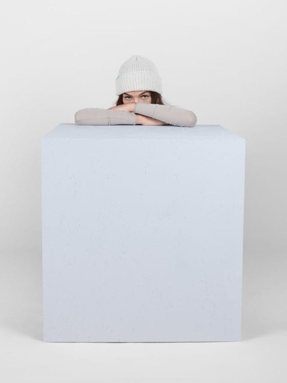 A woman wearing a beanie kneeling behind a cube with her upper torso leaning over the block