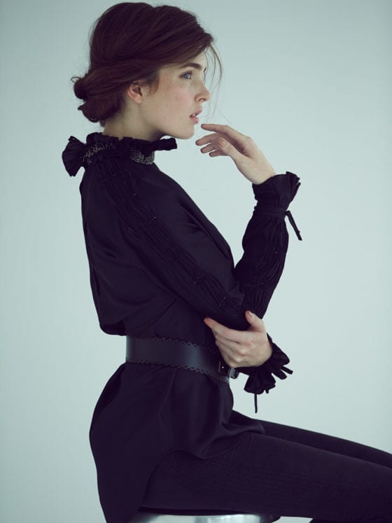 A side profile of a woman in all black seated on a stool