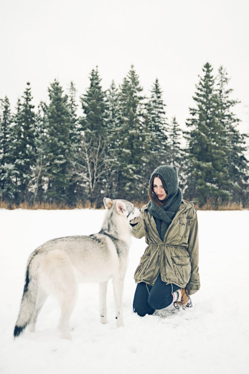 A woman kneeling in the snow as she pets her dog