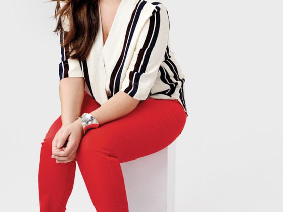 A woman in red pants and a striped shirt sitting on a cylinder shaped box