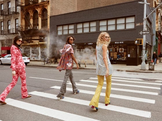 Three posh women crossing a New York Street as they look over their shoulders and back at the camera