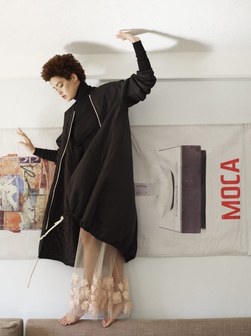 A woman standing on the backboard of a couch as she touches the ceiling