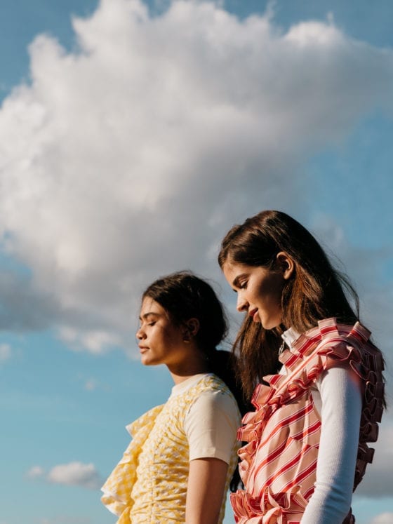 Two women standing side by side outside under the clouds