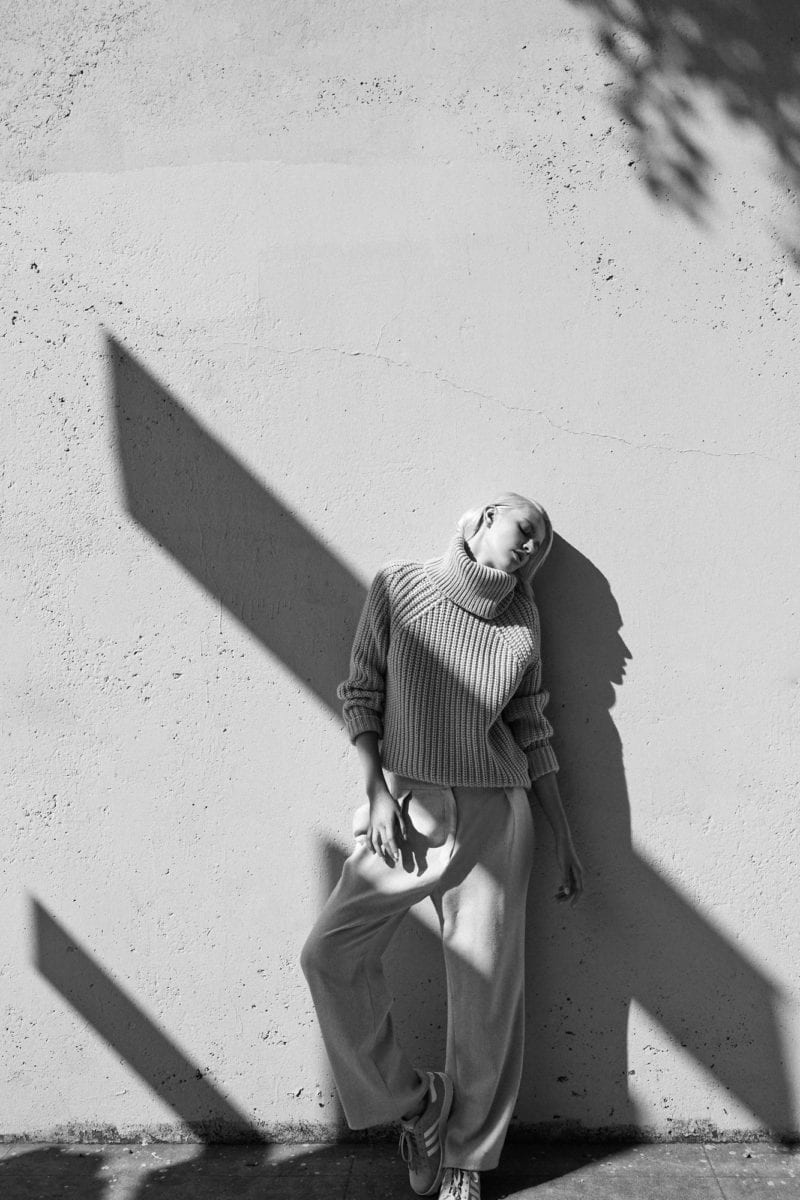 A black and white photo of a woman leading against a wall with a shadow covering her